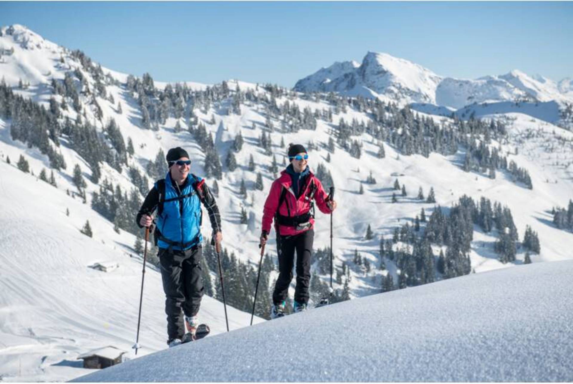 Two ski tourers can be seen in front of a snow-covered hill.