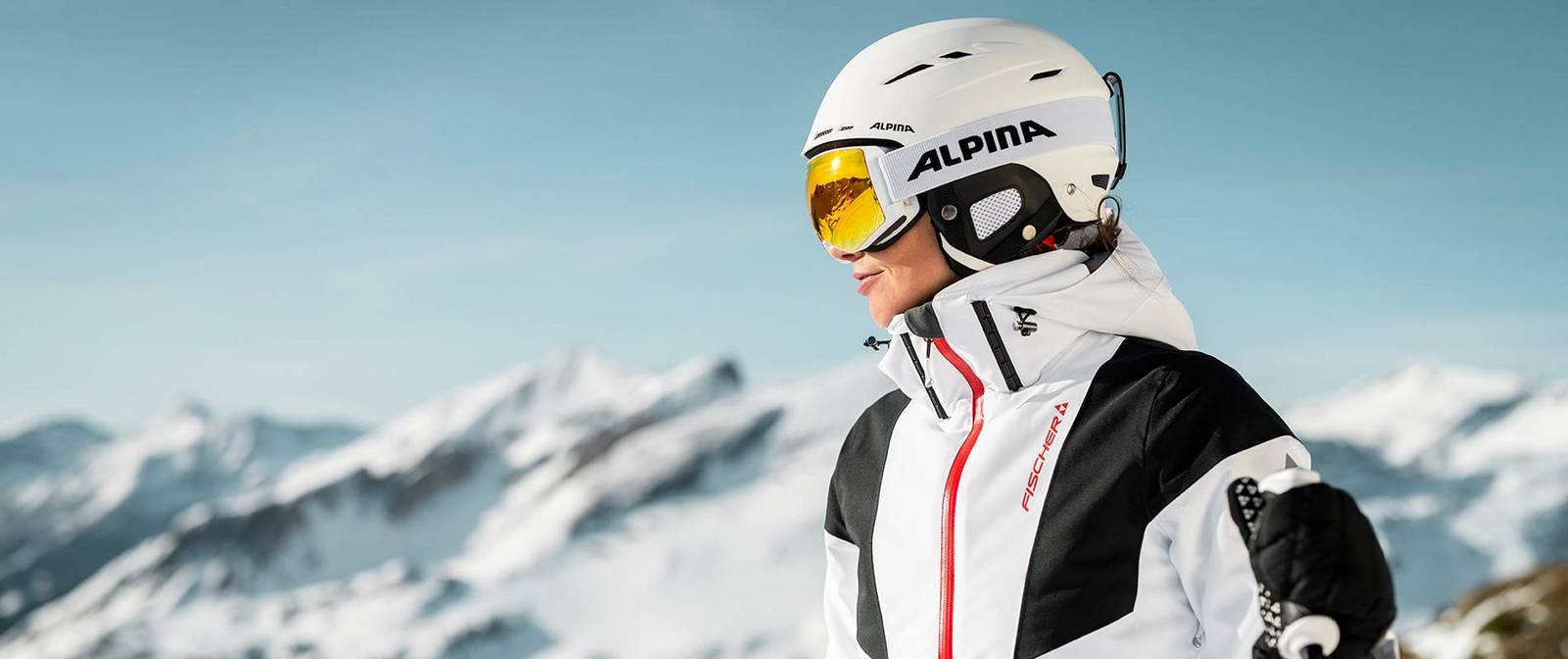 Eine Skifahrerin steht am Berg oben und wirft einen Blick ins Tal, bevor sie sich die Piste hinunter schwingt.