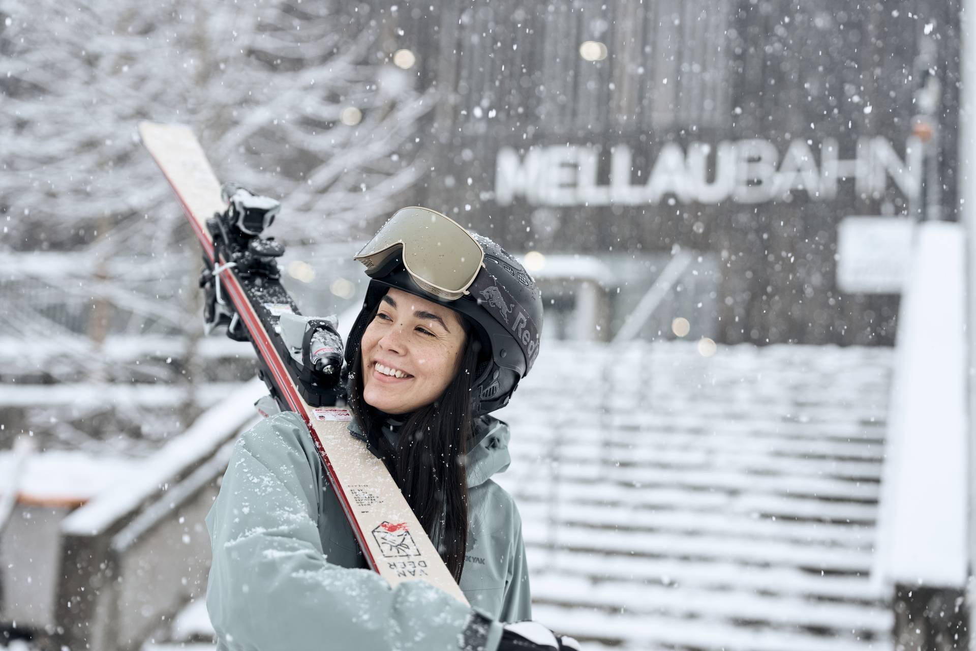 Skiier carries her skis on her shoulder, standing in front of the Mellaubahn lift
