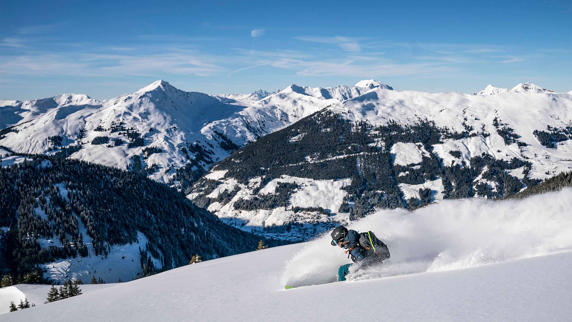 A skier races down the slope at high speed, kicking up snow behind him.