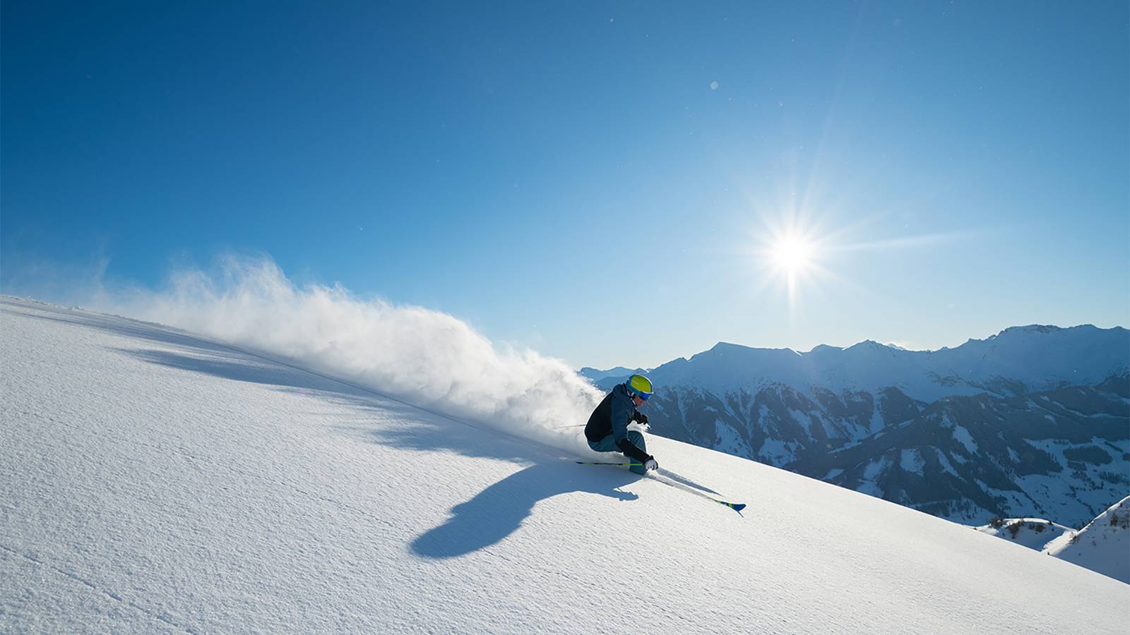 Ein Skifahrer fahrt mit vollem Tempo die Piste hinunter und wirbelt dabei Schnee hinter sich auf.