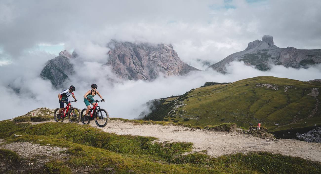 Zwei Mountainbiker fahren dem Trail entlang mit Bergpanorama.