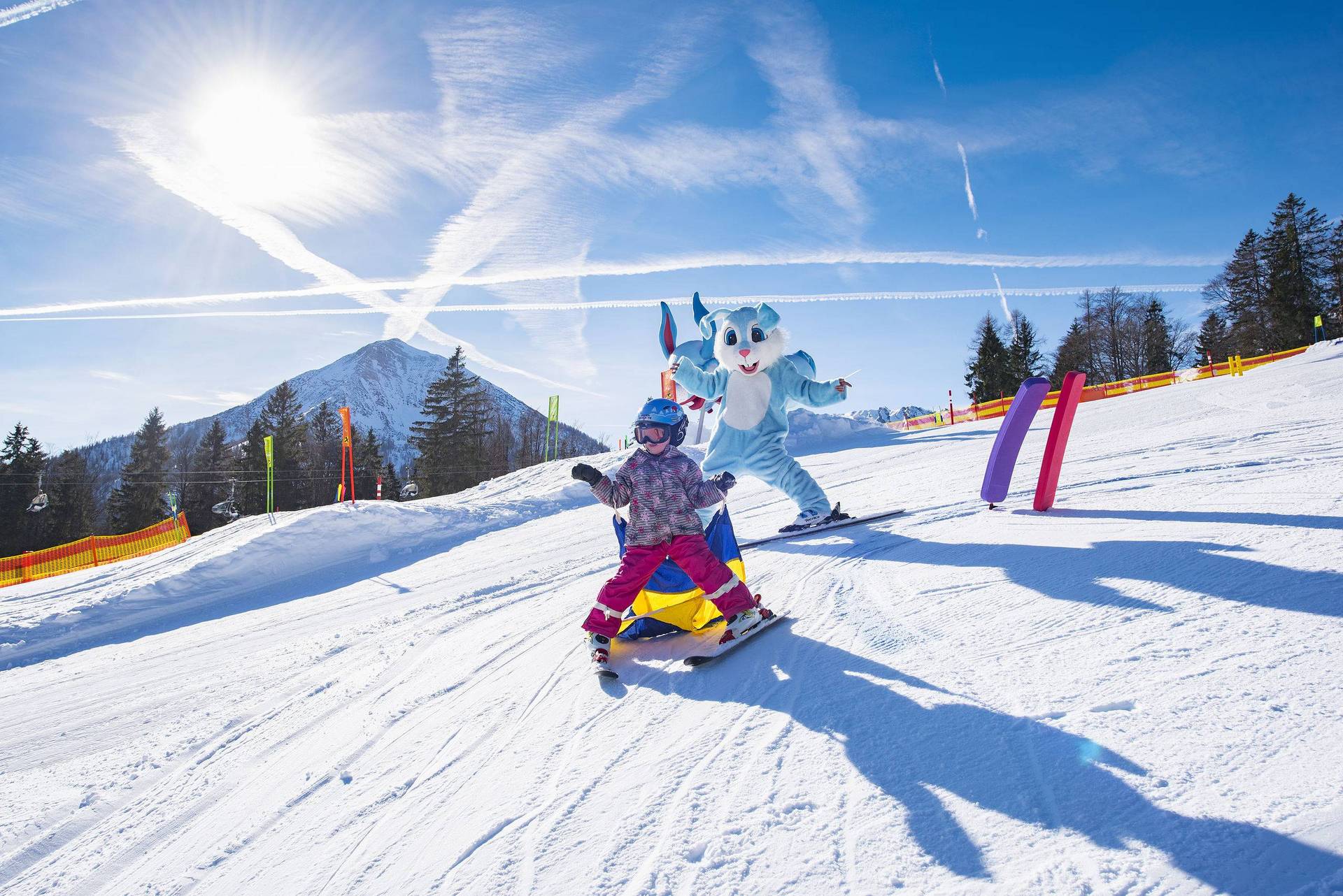 Een kind skiet met de mascotte de piste af.