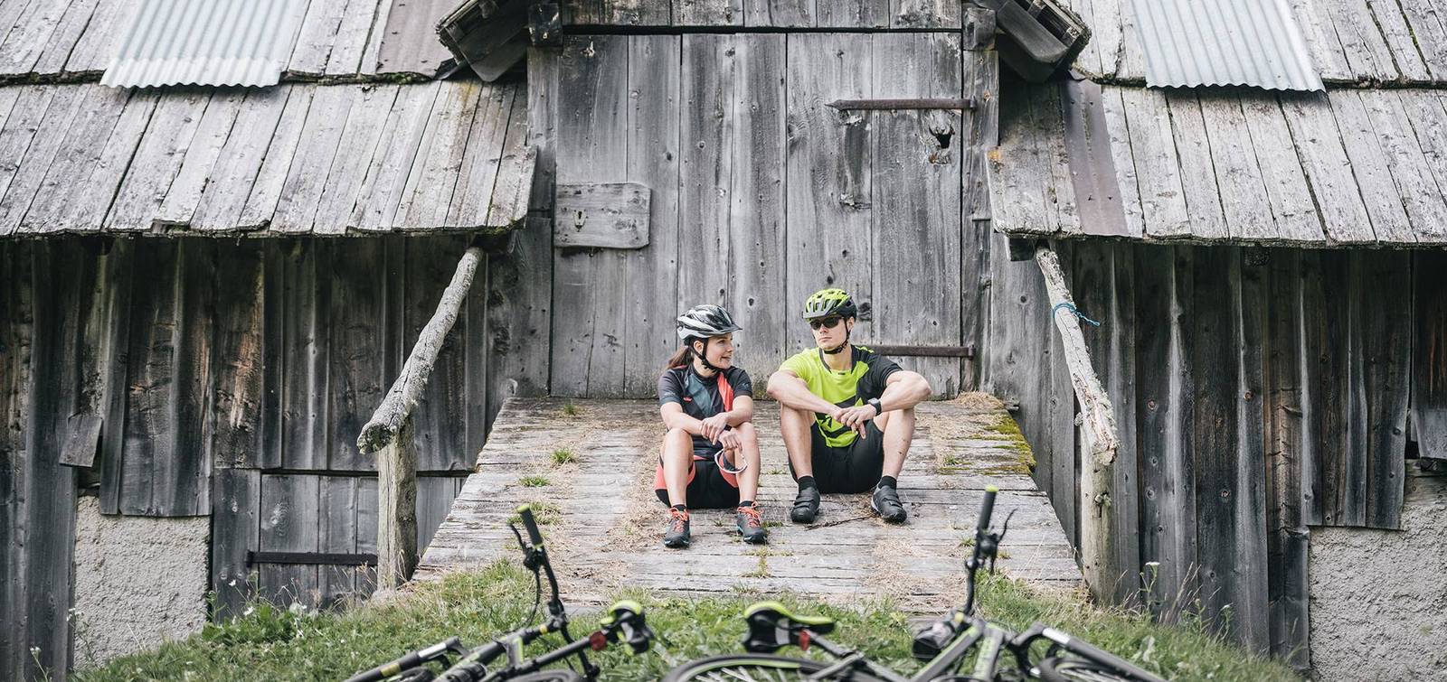Zwei Mountainbiker die gerade eine Pause vor einer alten Hütte machen.