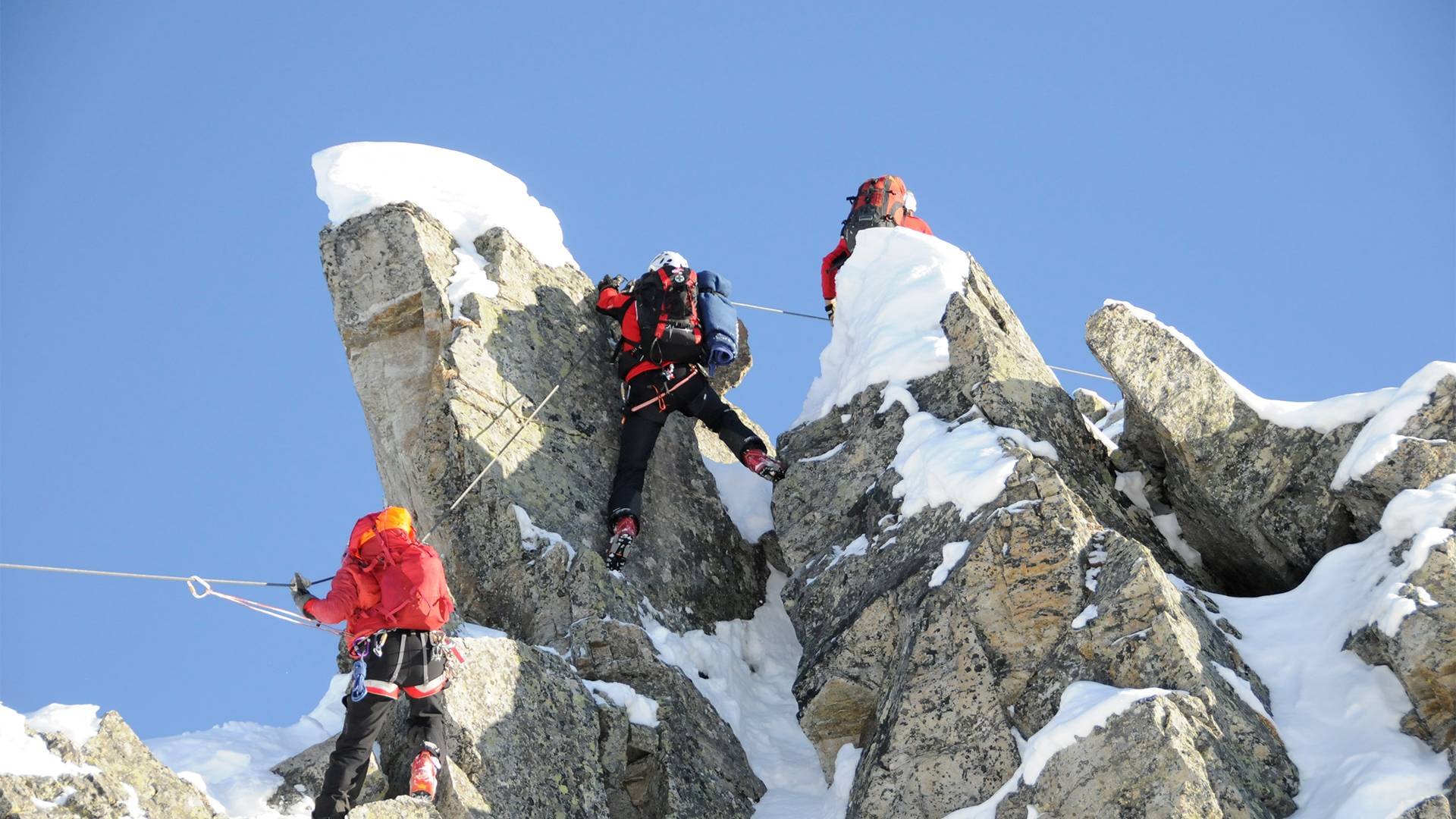 Drei Personen klettern auf einem Winterklettersteig.