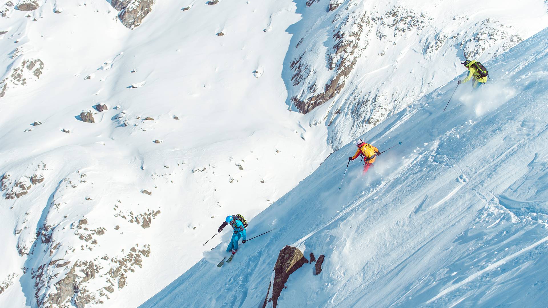 Several people happily ski down a steep slope.