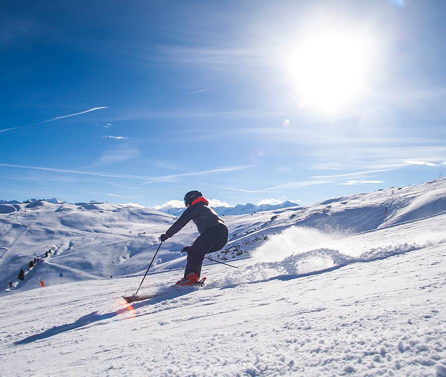Ein Skifahrer fährt vor strahlend blauem Himmel die Piste hinunter.
