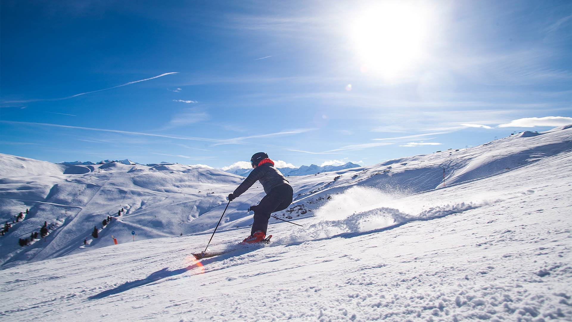 Een skiër daalt onder een stralend blauwe hemel de piste af.