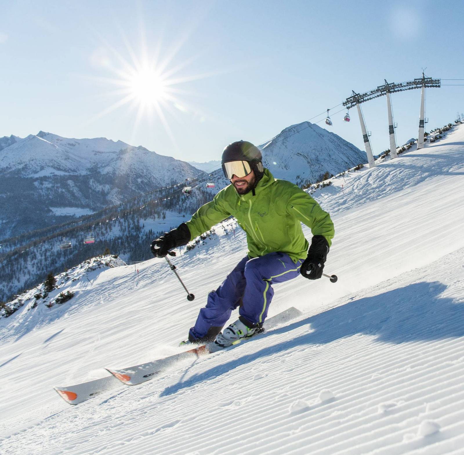 Ein Skifahrer mit einer grünen Jacke fährt auf einer frisch präparierten Piste.
