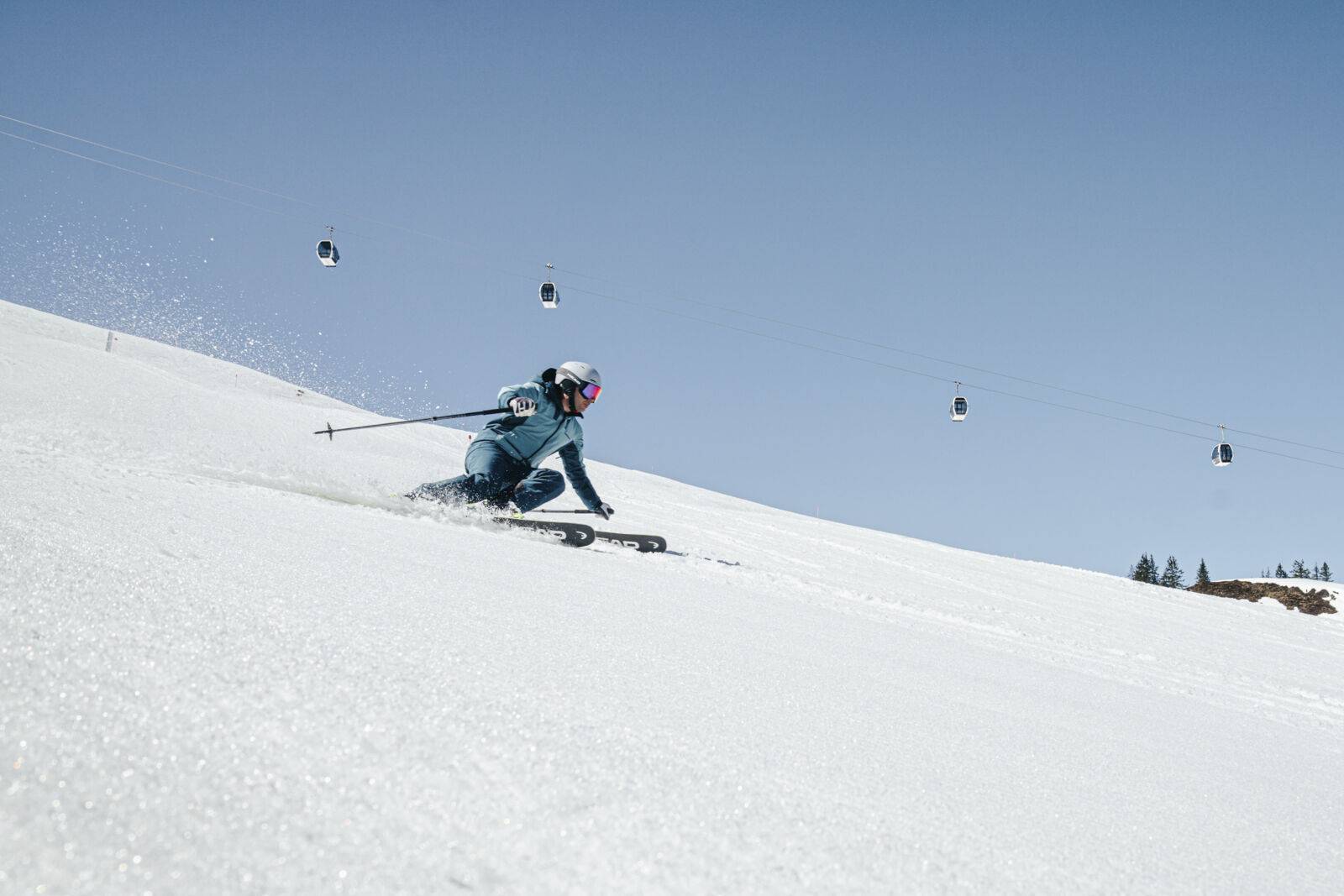 Skifahrerin fährt auf der Skipiste, im Hintergrund ist die Gondelbahn zu sehen