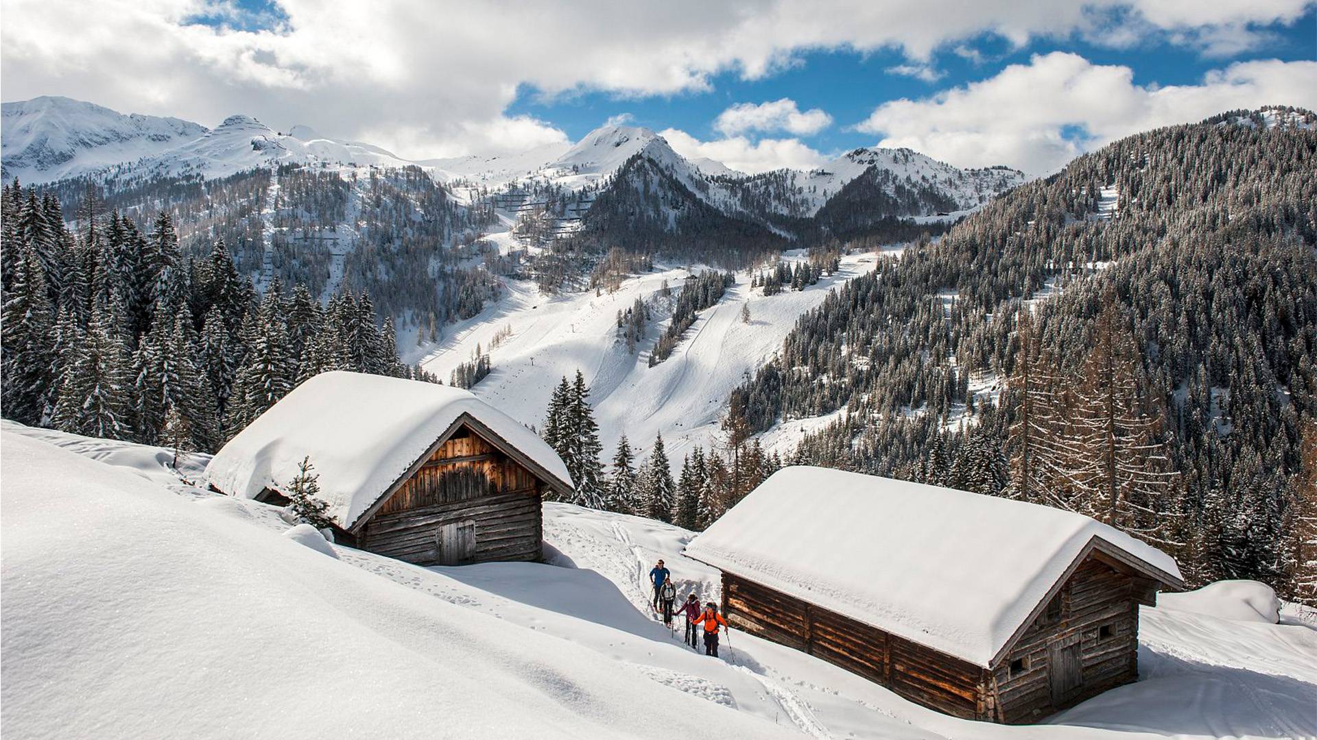 Four ski tourers make their way up the mountain, away from the slopes and huts