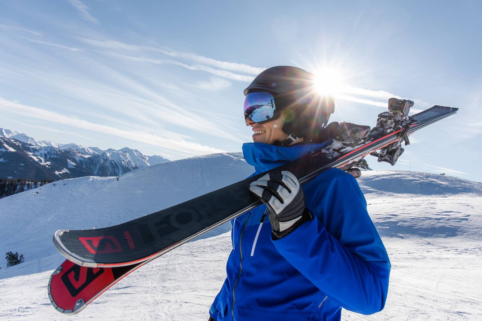 Glücklicher Skifahrer trägt seinen Salomon Skier auf der Schulter.