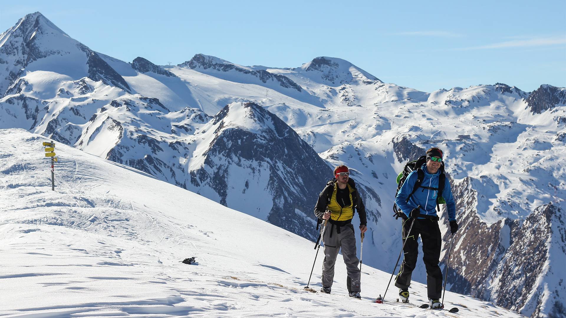 Twee skiërs wandelen lachend naar de top.