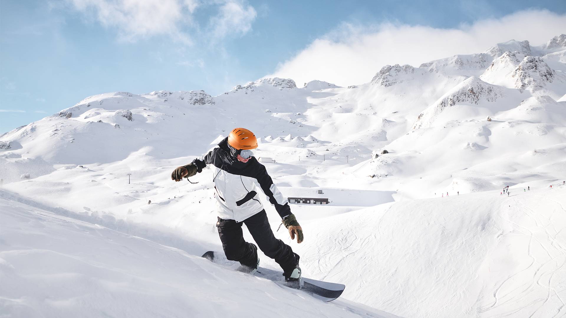A snowboarder rides down the perfectly groomed slope against a beautiful mountain backdrop