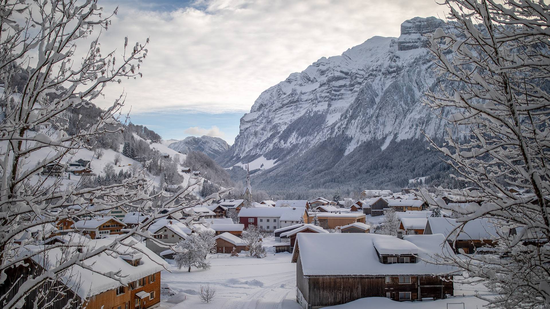 Een dorpsbeeld van het besneeuwde Mellau, met op de achtergrond bergen.