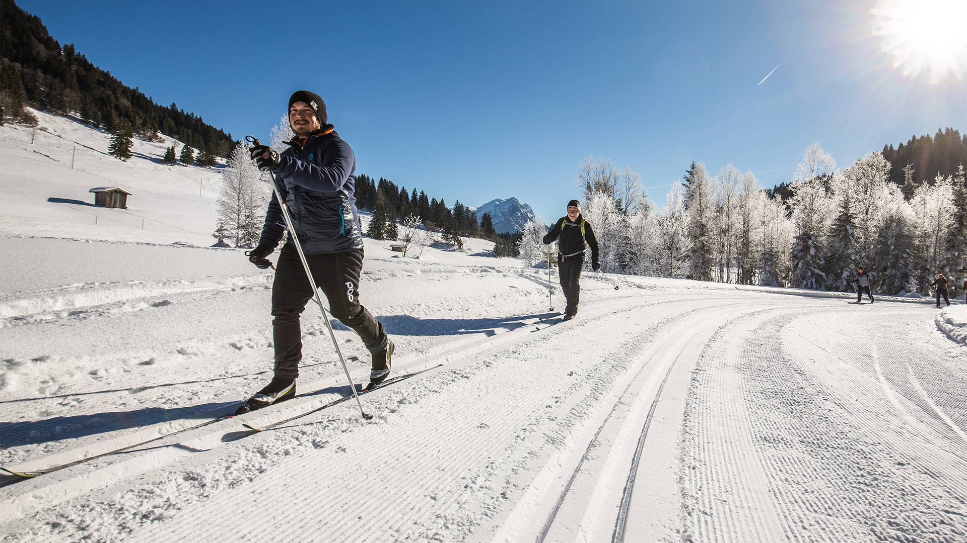 Twee langlaufers skiën achter elkaar op een recht stuk.