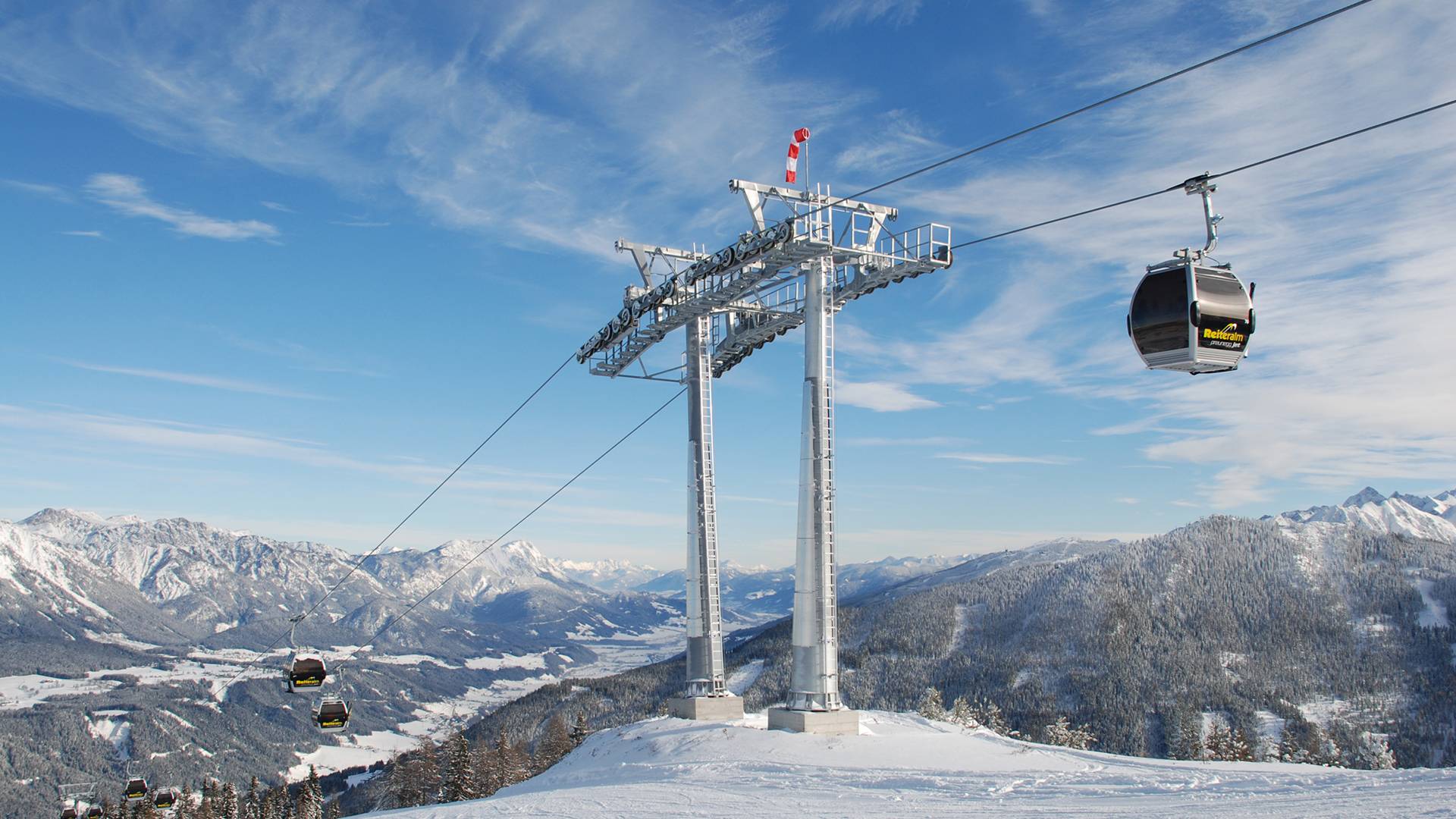A gondola ascends the mountain against a bright blue sky.