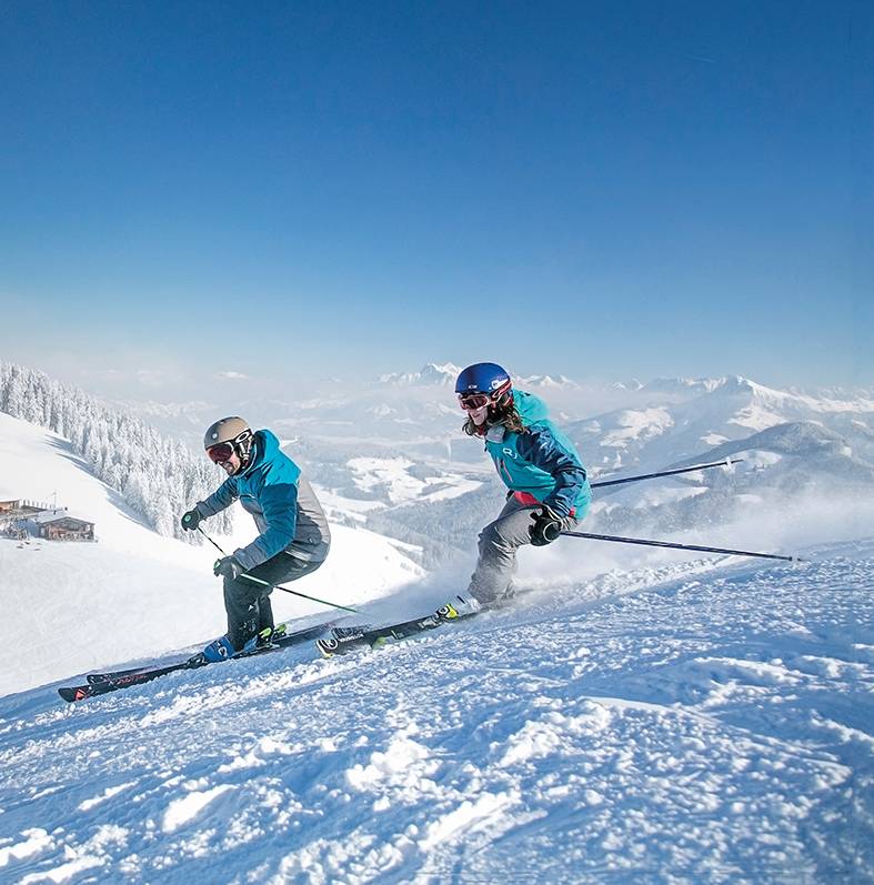 Zwei Skifahrer fahren hintereinander die Piste hinunter.