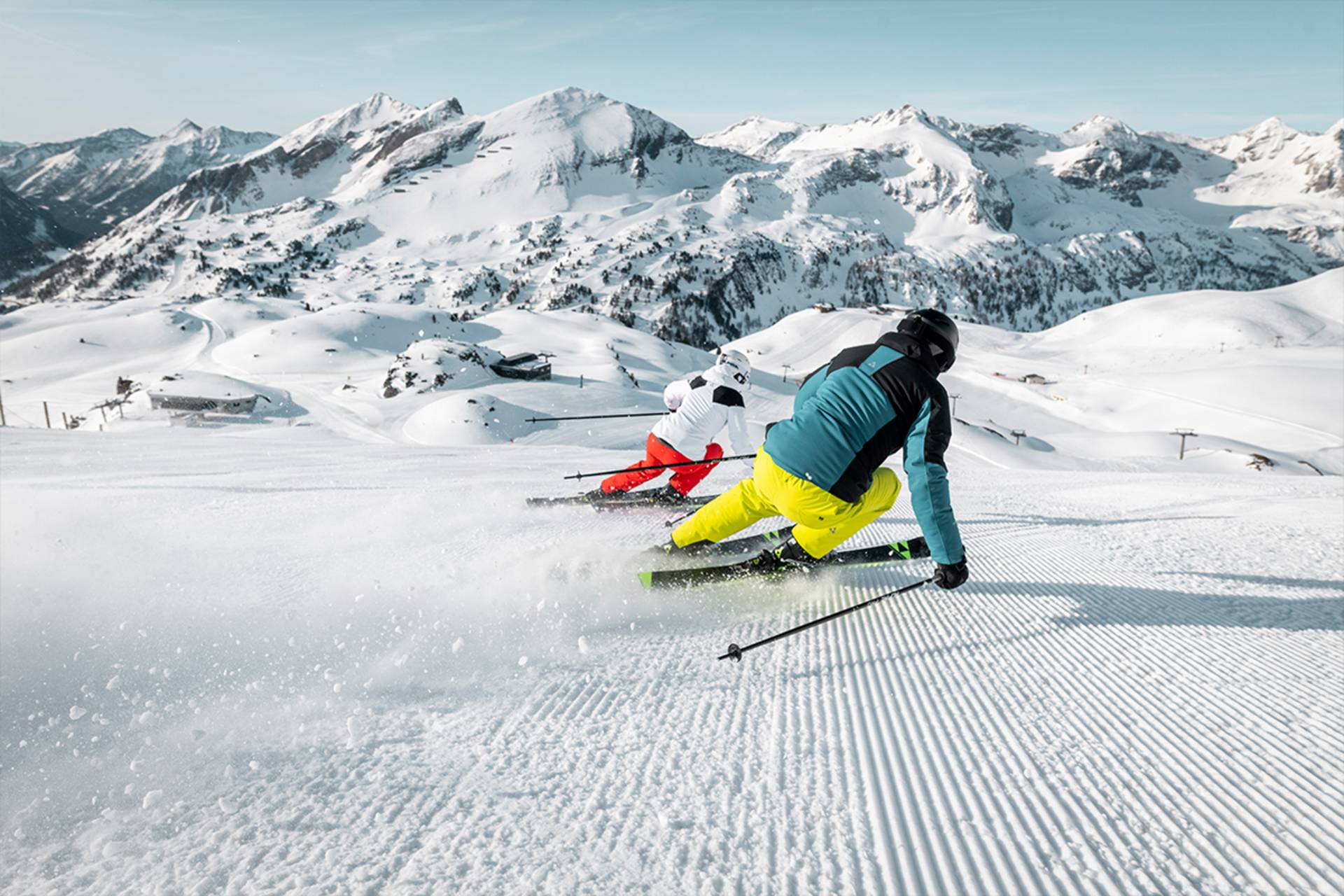 Je ziet twee skiërs op de piste naar beneden skiën.