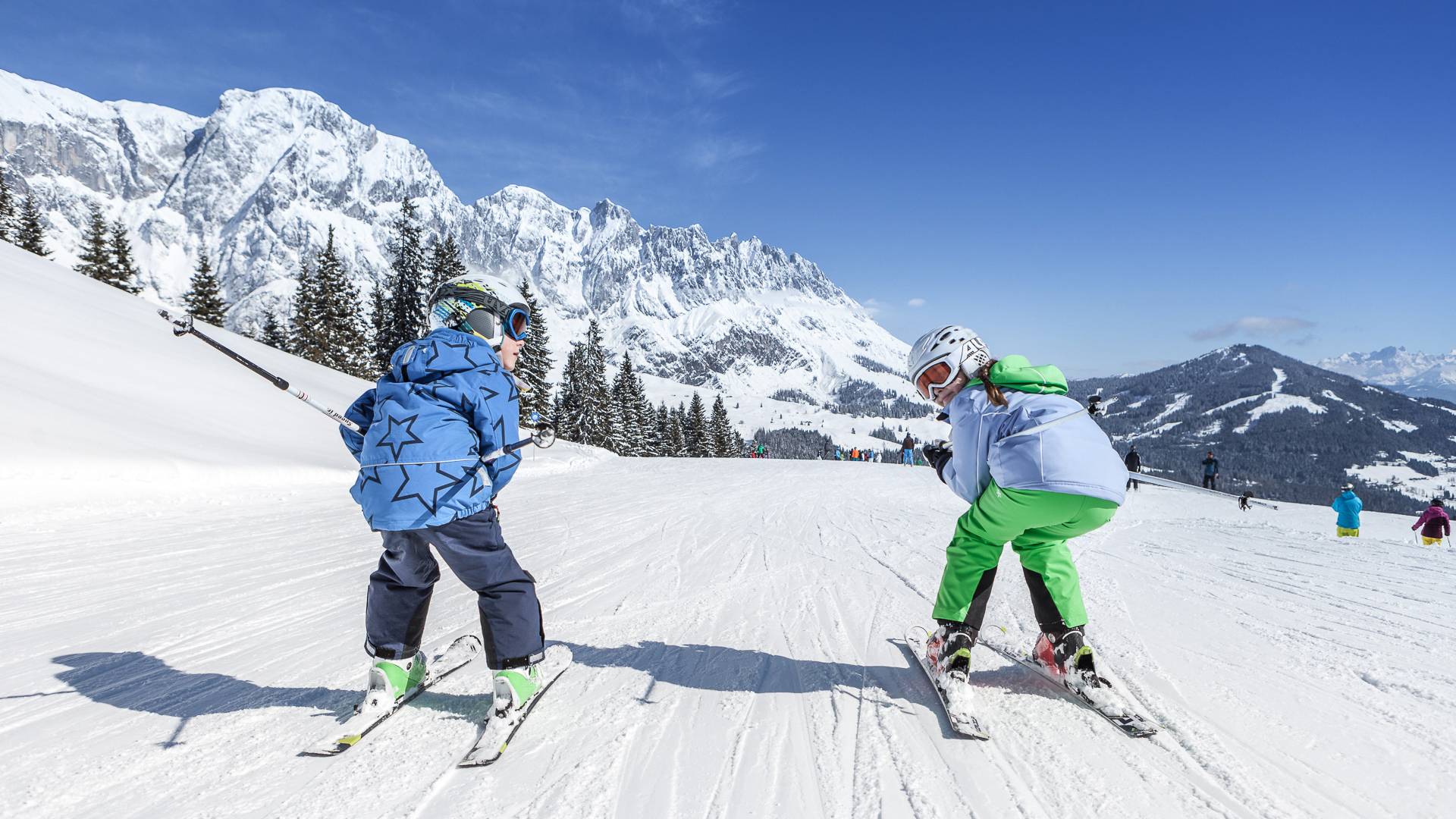 Two people skiing down the mountain in a crouched position.
