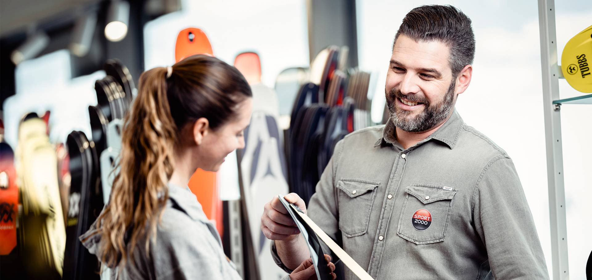 Een medewerker adviseert een klant voor een rek en houdt daarbij een ski in zijn hand.
