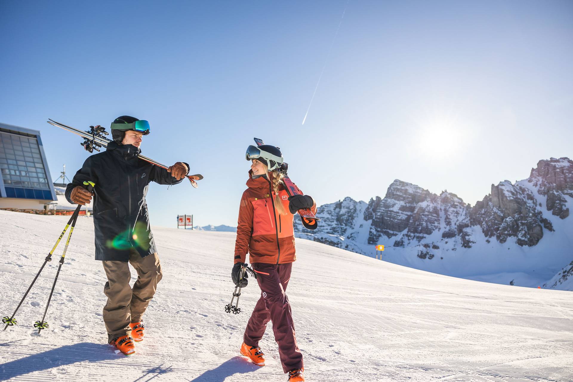 Zwei Skifahrer tragen ihre Ski auf der Schulter neben der Bergstation