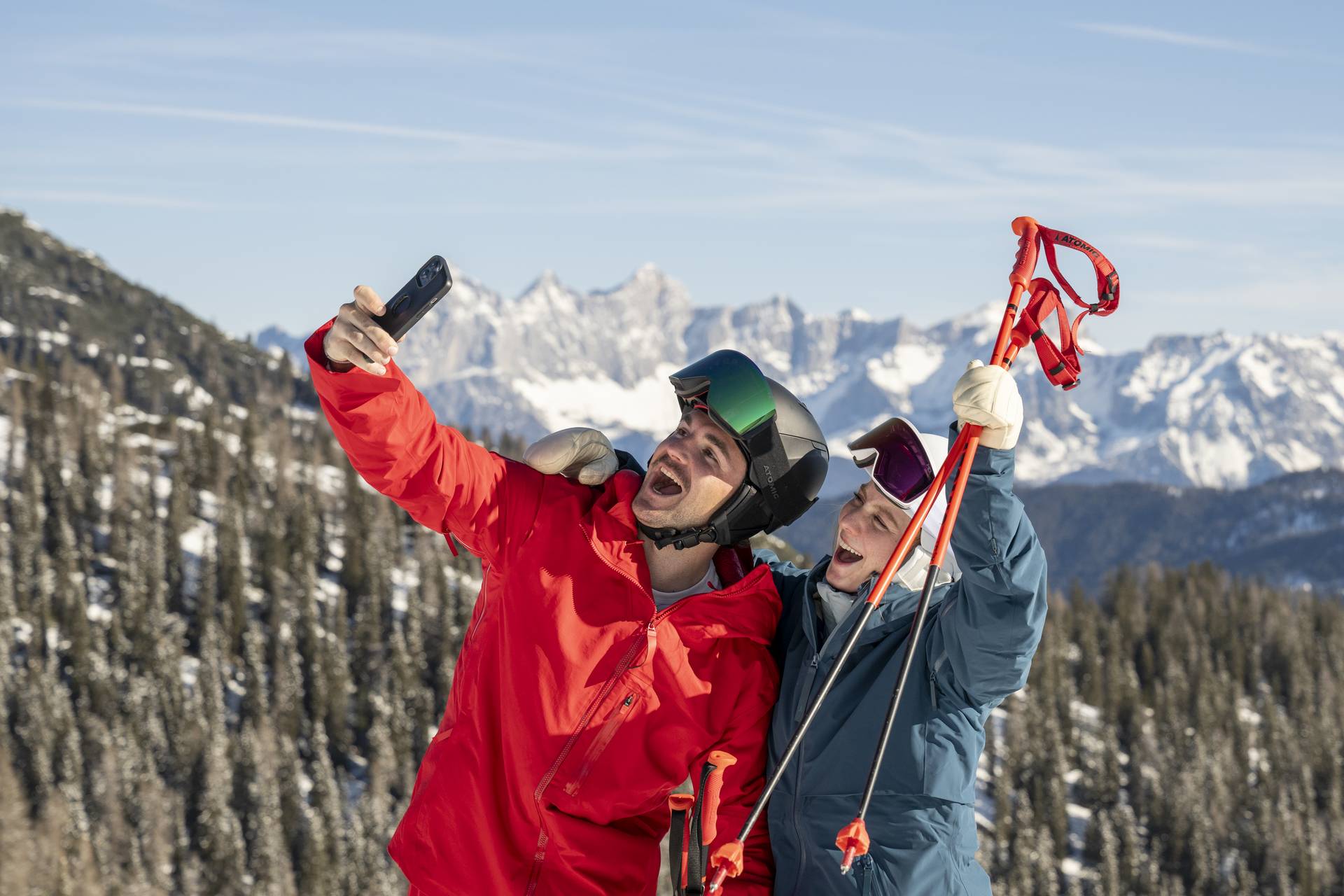 Pärchen macht ein Selfie auf der Skipiste, beide lachen.