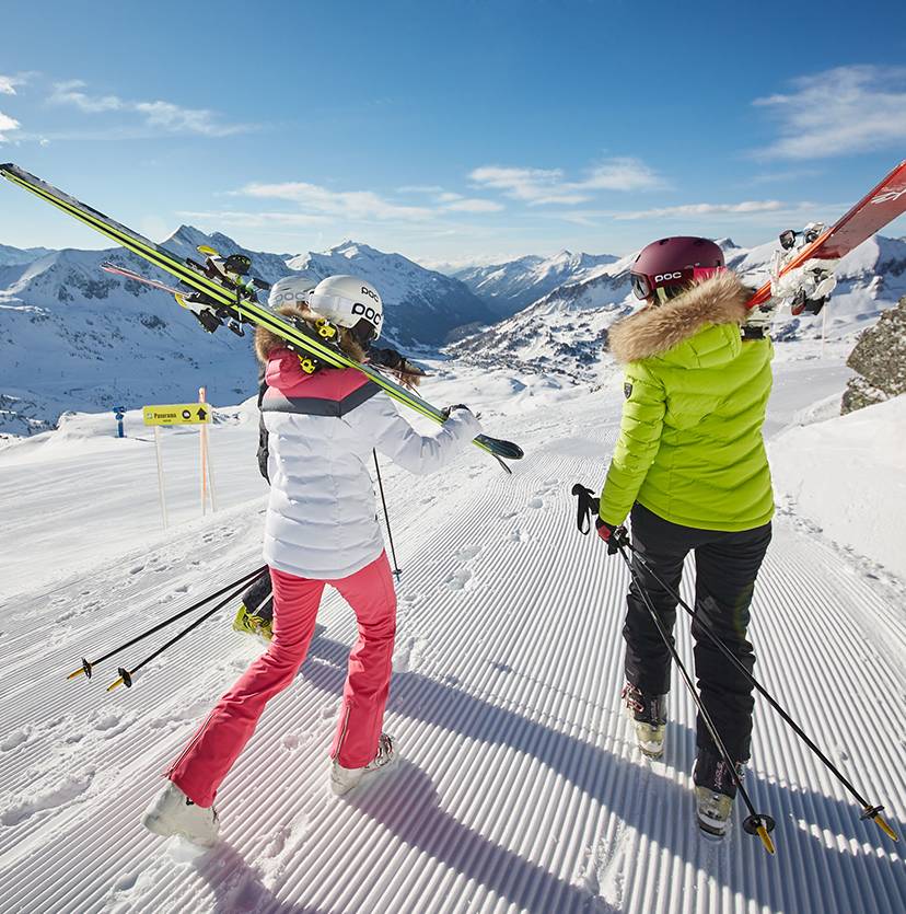 Zwei Personen wandern mit den Ski auf den Schultern einen präparierten Weg entlang.