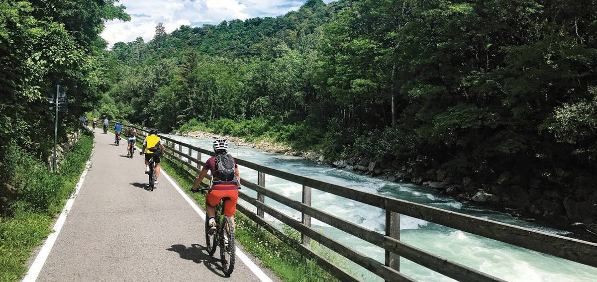 Eine Gruppe von Radfahrern die in Südtirol neben einem Fluss fahren.