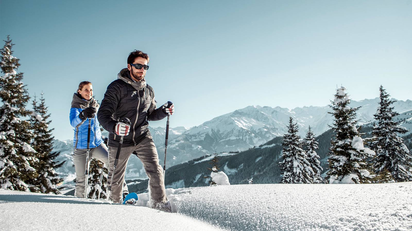 Eine Aufnahme von zwei Schneeschuh Wanderern die die atemberaubende Aussicht über die Winterlandschaft sichtlich genießen.