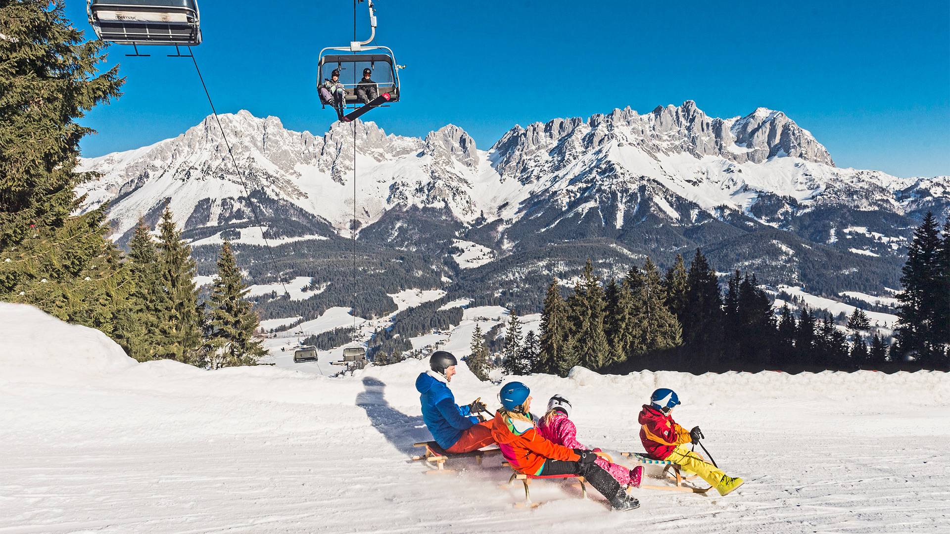 A family sledging with a chairlift visible in the background.