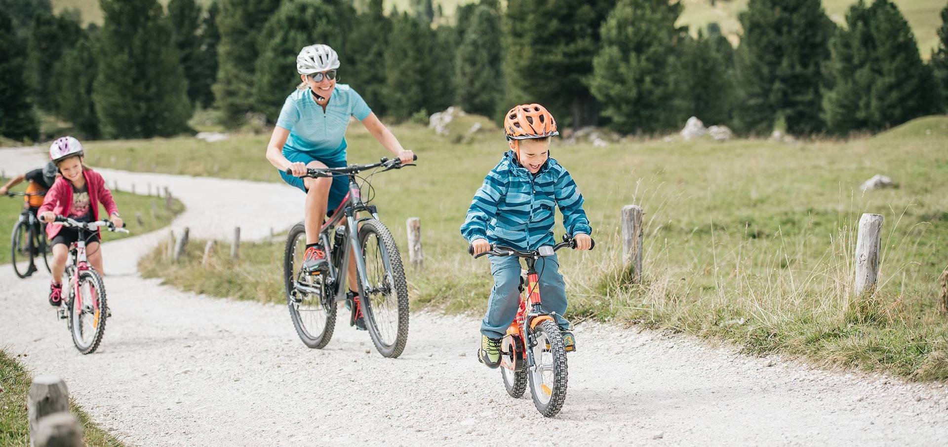 Familie mit 2 Kindern fährt mit dem Rad freudestrahlend einen Weg entlang.