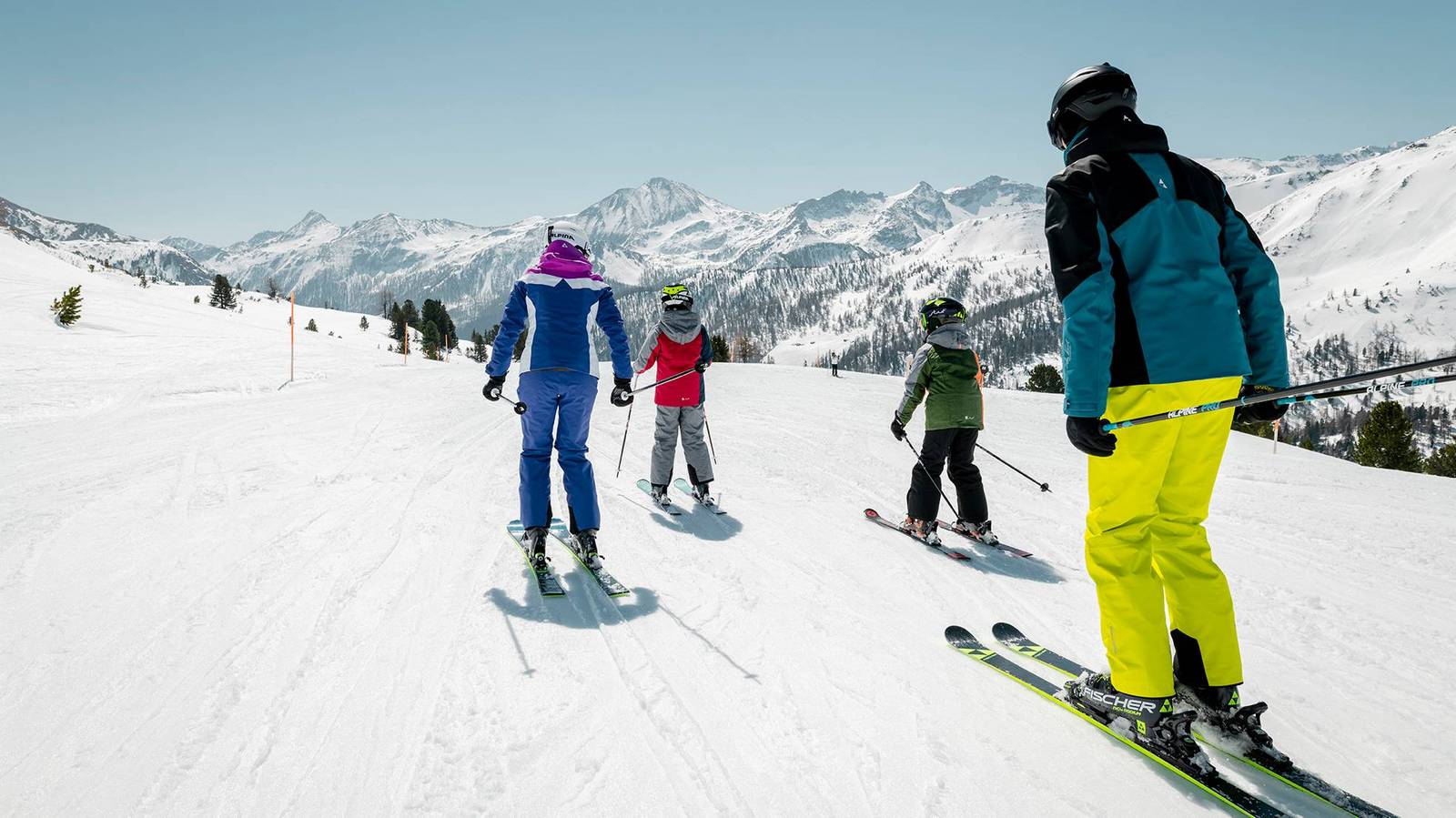 Eltern und Kinder fahren zusammen auf einer leichten Skistrecke.