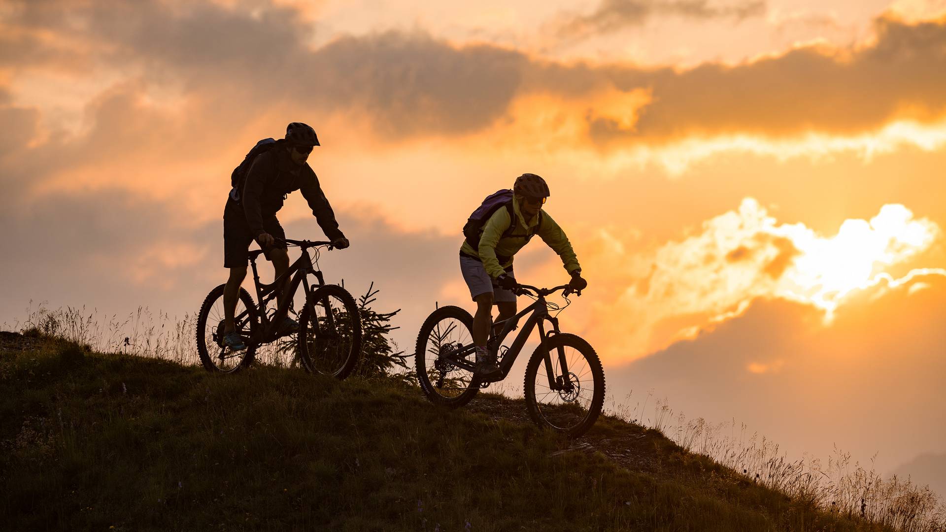 Ein Pärchen fährt mit den Mountainbikes bei Sonnenuntergang hinunter ins Tal.
