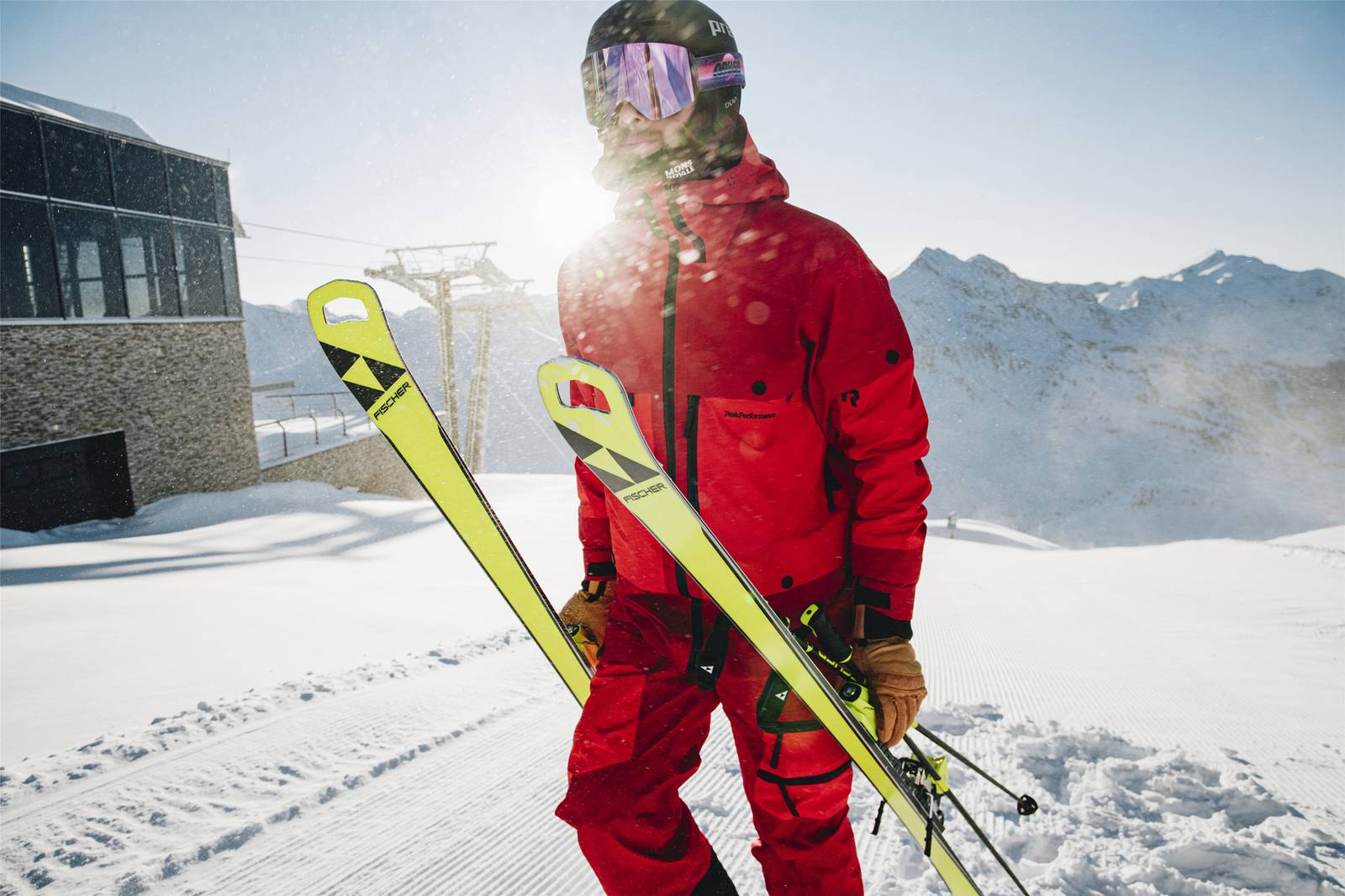 Skifahrer hält seine Skier in der Hand und sieht in die Ferne.