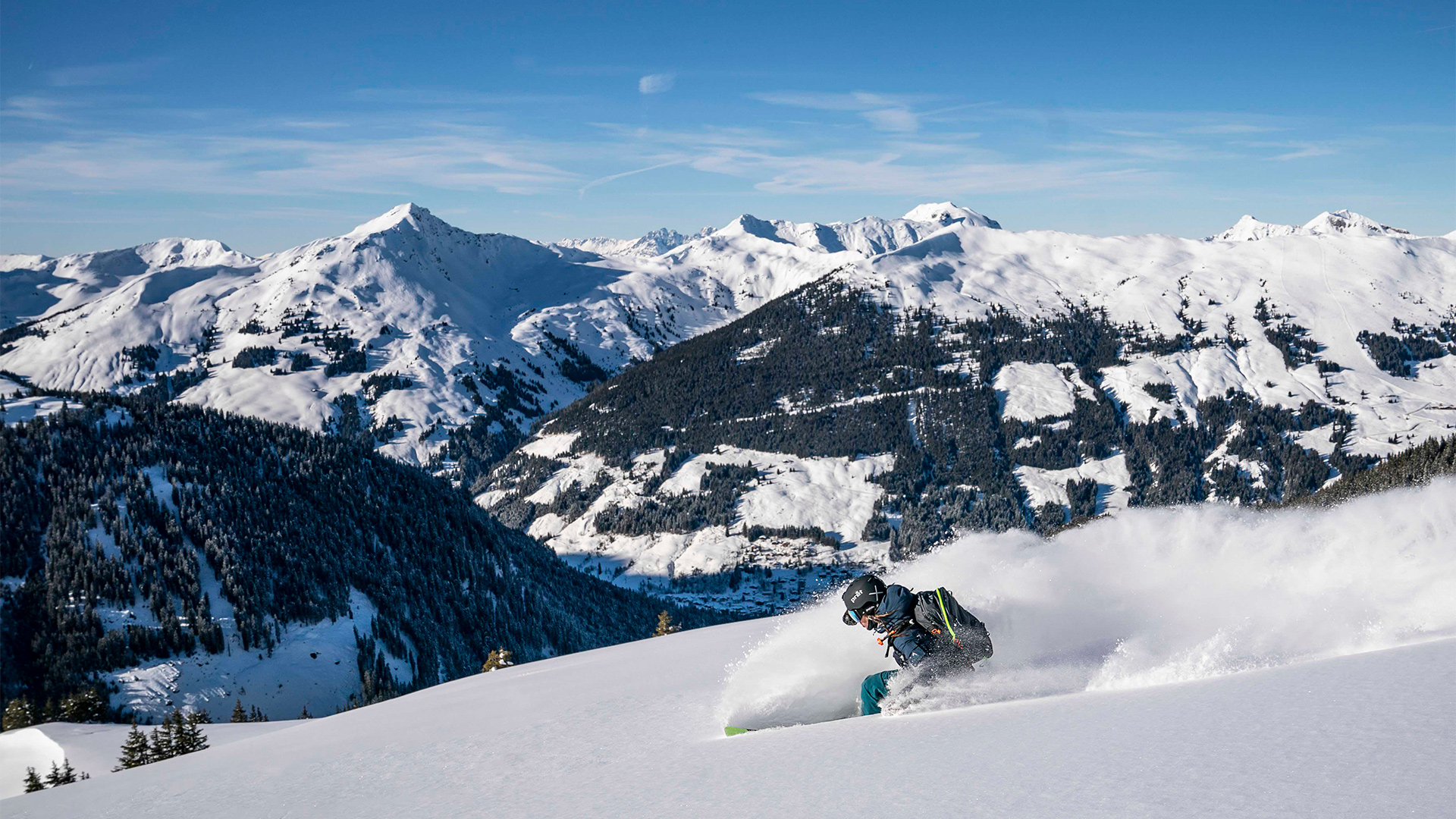 Ein Skifahrer fährt mit hohem Tempo die Piste hinunter und wirbelt dabei Schnee hinter sich auf.